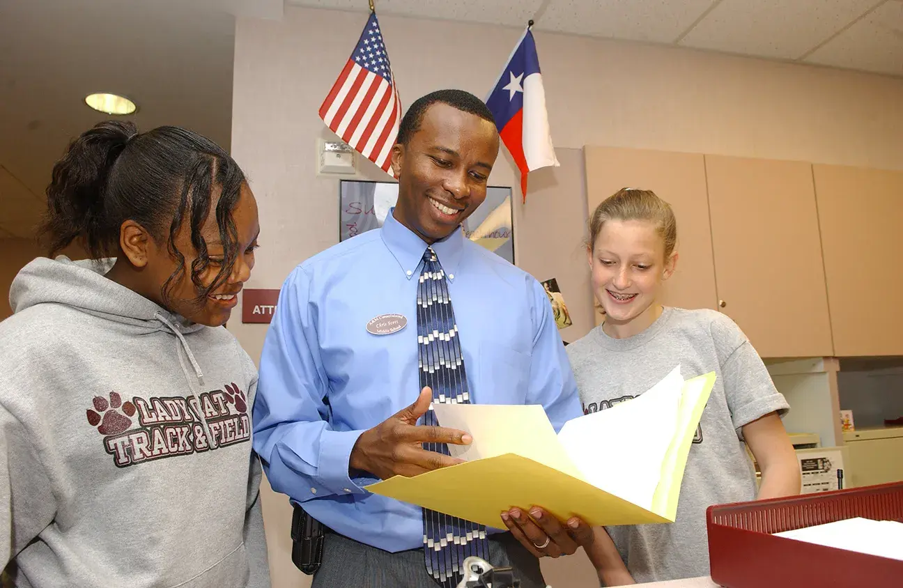 An administrator reviews a document with two students